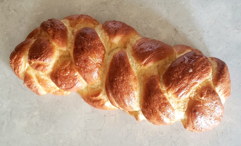 Puede incluir: Una hogaza de pan trenzado con una corteza dorada. El pan est&aacute; horneado a la perfecci&oacute;n y tiene un glaseado brillante.