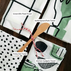 Pu&ograve; includere: Quattro asciugamani da cucina con diversi design. Il primo asciugamano ha un motivo a quadri verde e nero. Il secondo asciugamano ha un'illustrazione verde e nera di un coltello, un cucchiaio e una forchetta. Il terzo asciugamano ha un motivo a pois neri. Il quarto asciugamano ha un'illustrazione verde e nera di utensili da cucina.