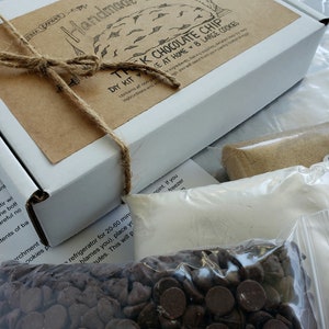 Pu&ograve; includere: Una scatola marrone con un'etichetta bianca che dice "Handmade for You" e "The Chocolate Chip DIY Kit - Make at Home 8 Large Cookies". La scatola &egrave; legata con uno spago e ha un sacchetto di gocce di cioccolato di fronte.