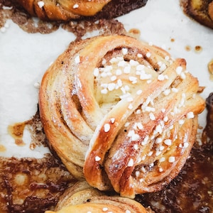 Op de afbeelding: Close-up van een kaneelrol met een swirl-ontwerp en een suikerglazuur. De rol is bedekt met witte sprinkles.