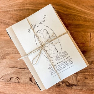 May include: A DIY kit for making 3 pullas, wrapped in a beige paper band and tied with twine. The kit includes instructions and non-perishable ingredients. The text on the packaging reads "Handmade by You" and "3 Pullas".