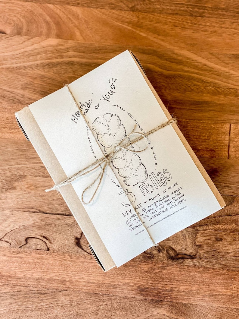 May include: A DIY kit for making 3 pullas, wrapped in a beige paper band and tied with twine. The kit includes instructions and non-perishable ingredients. The text on the packaging reads "Handmade by You" and "3 Pullas".