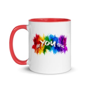 May include: White ceramic coffee mug with a red rim and handle. The mug features a rainbow-colored paint splatter design with the text "BE YOU TIFUL" in white.