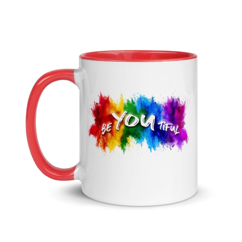 May include: White ceramic coffee mug with a red rim and handle. The mug features a rainbow-colored paint splatter design with the text "BE YOU TIFUL" in white.