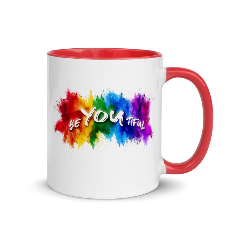 May include: White ceramic coffee mug with a red rim and handle. The mug features a colorful rainbow explosion with the text "Be You Tiful" in white.
