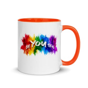 May include: White ceramic coffee mug with an orange rim and handle. The mug features a colorful rainbow explosion with the text "Be You Tiful" in white.