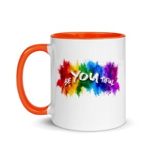 May include: White ceramic coffee mug with an orange rim. The mug features a rainbow-colored powder explosion with the text "BE YOU TIFUL" in white.