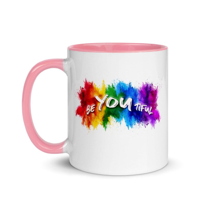 May include: White ceramic mug with a pink rim. The mug features a rainbow-colored paint splatter design with the text "BE YOU TIFUL" in white.