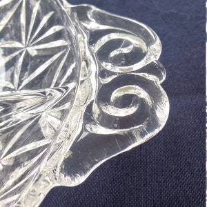 Pu&ograve; includere: Un piatto da portata in vetro trasparente con un bordo ondulato e un motivo a diamante sul fondo. Il piatto ha un design decorativo a spirale attorno al bordo.