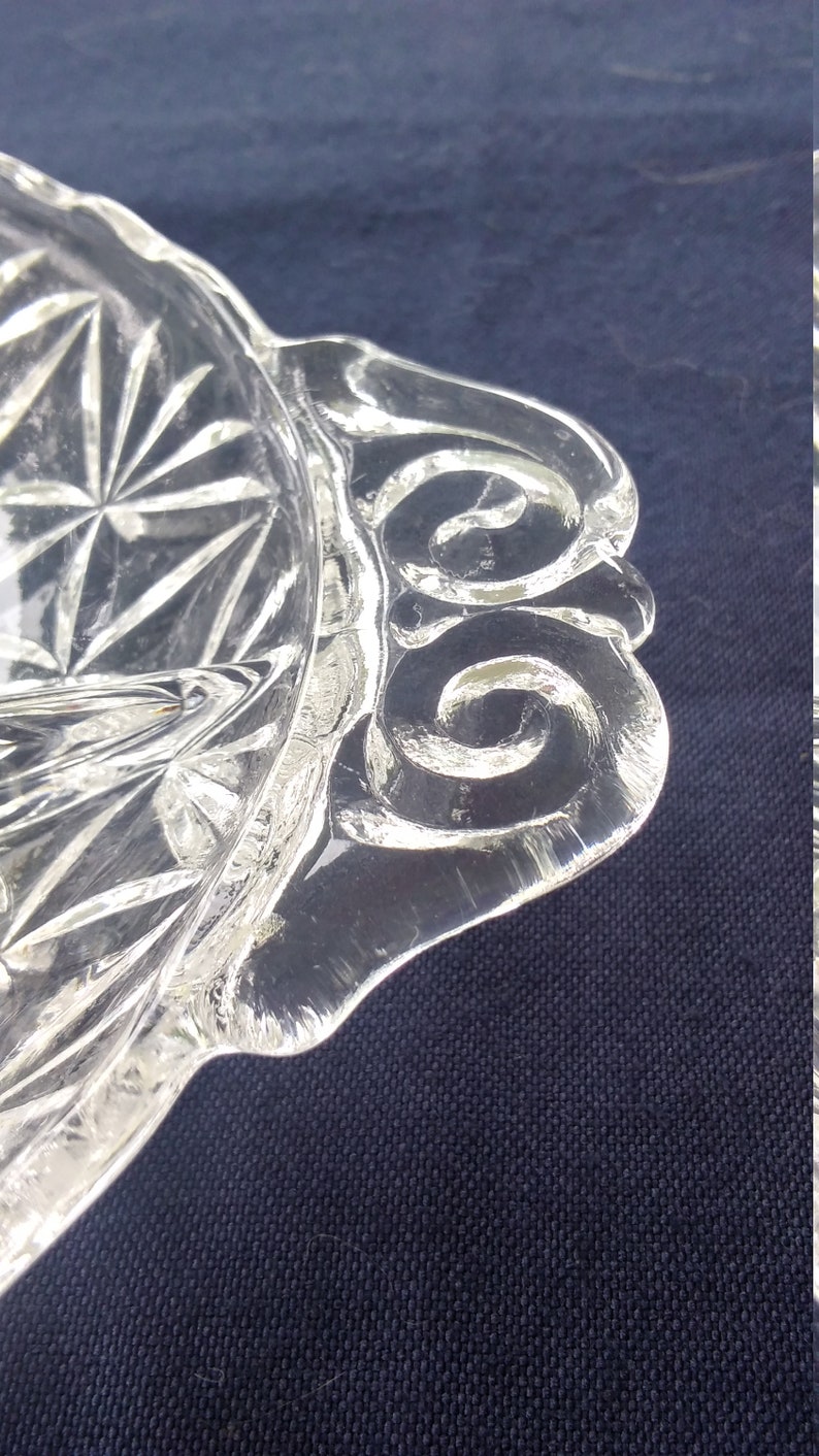 Pu&ograve; includere: Un piatto da portata in vetro trasparente con un bordo ondulato e un motivo a diamante sul fondo. Il piatto ha un design decorativo a spirale attorno al bordo.