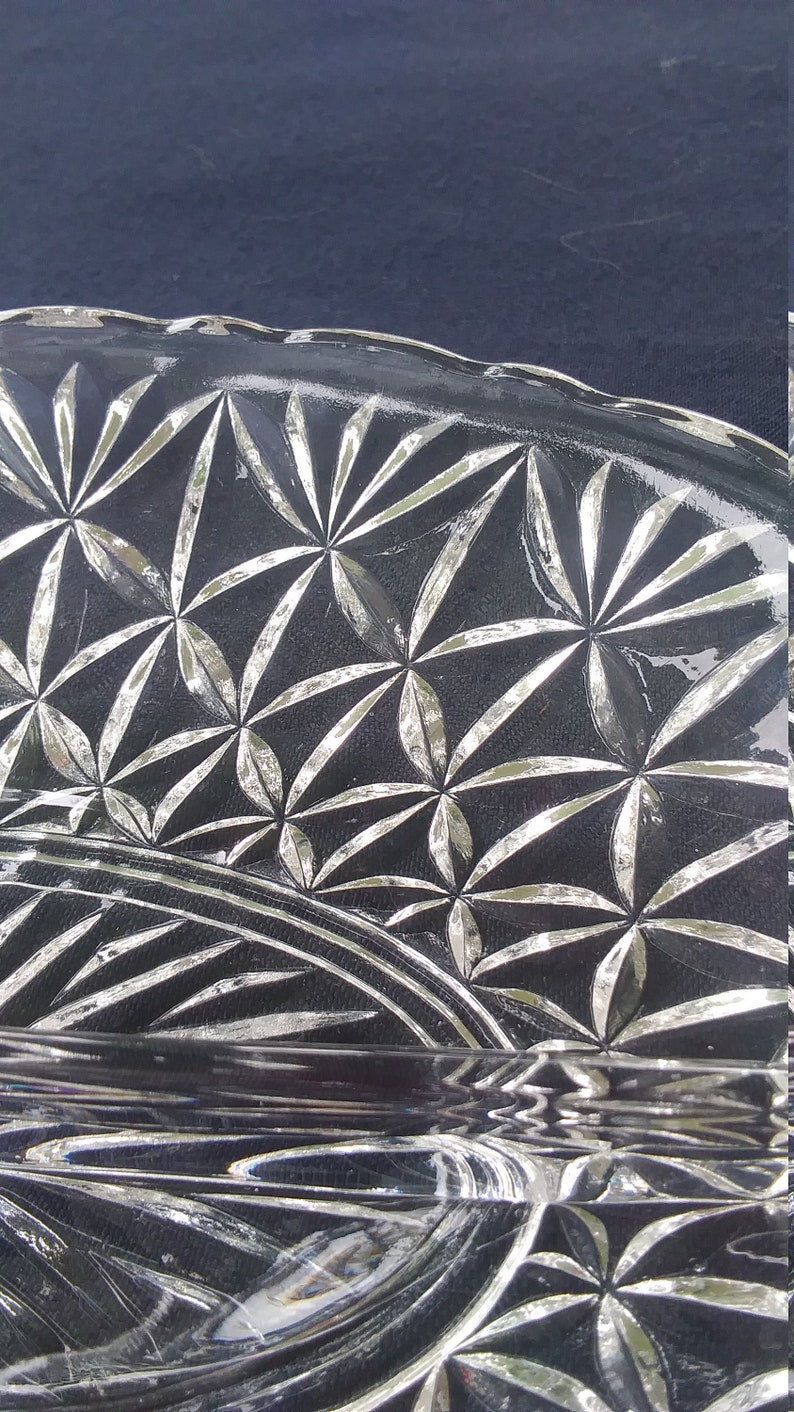 Pu&ograve; includere: Un piatto da portata in vetro trasparente con un motivo decorativo in vetro tagliato. Il motivo presenta un disegno ripetitivo di stelle e linee.