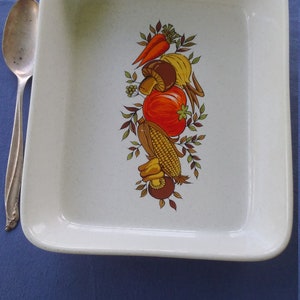 May include: White ceramic baking dish with a brown, yellow, orange, and green vegetable design. The design features a carrot, corn, tomato, and mushrooms.