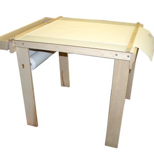 May include: A wooden art table with a roll of paper and a tray for supplies. The table is made of light wood and has a simple design.