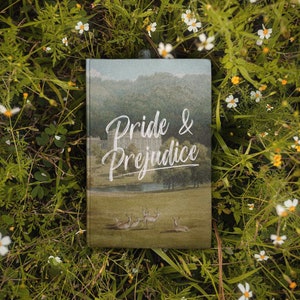 May include: A green book with a landscape scene on the cover. The title "Pride & Prejudice" is written in white cursive font.