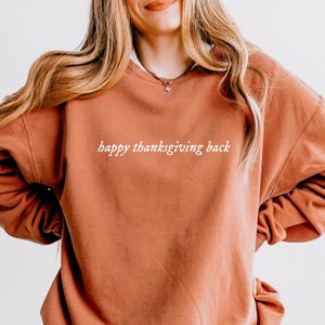 Può includere: Una felpa color ruggine con la scritta "happy thanksgiving back" in lettere bianche.