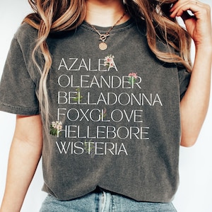 May include: A gray t-shirt with a white graphic print of the words "Azalea", "Oleander", "Belladonna", "Foxglove", "Hellebore", and "Wisteria".