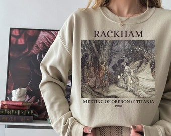 Puede incluir: Una sudadera beige con un estampado gráfico de una ilustración en blanco y negro de hadas en un bosque. El texto "RACKHAM" está impreso sobre la ilustración y "MEETING OF OBERON & TITANIA 1908" está impreso debajo de la ilustración. La modelo lleva una falda a cuadros.