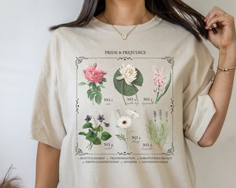 May include: A beige oversized t-shirt with a graphic print of flowers and the text "PRIDE & PREJUDICE". The graphic includes six different flowers with numbers and names, such as "water lily" and "lavender". Below the graphic is a list of character traits associated with each flower.