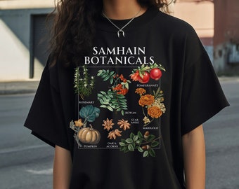 May include: Black t-shirt with a graphic print of botanical illustrations and the text "Samhain Botanicals". The illustrations include rosemary, rowan, pomegranate, star anise, marigold, pumpkin, oak and acorns.