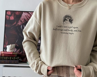 May include: A beige sweatshirt with a graphic print of a woman and the text "I wish I were a girl again, half-savage and hardy, and free. -Wuthering Heights". The sweatshirt is paired with a brown and white plaid skirt.