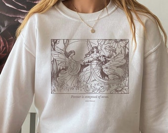 Puede incluir: Sudadera blanca con un estampado gráfico marrón de tres hadas con alas y flores. El gráfico incluye el texto "Forever is composed of nows." - Emily Dickinson.