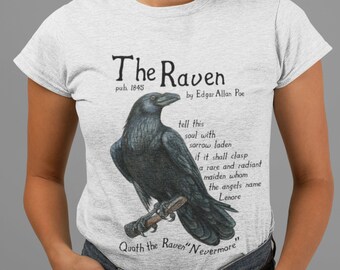 Puede incluir: Una camiseta gris con una ilustración de cuervo negro y el texto "The Raven" de Edgar Allan Poe, publicado en 1845. El texto también incluye una cita del poema: "Quoth the Raven 'Nevermore'."