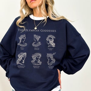 May include: Navy blue sweatshirt with a white graphic print of the Olympian Goddesses. The graphic features the names and attributes of each goddess: Hera, Hestia, Athena, Aphrodite, Demeter, and Artemis.