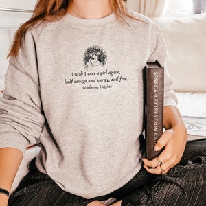 May include: A gray sweatshirt with a quote from Wuthering Heights: "I wish I were a girl again, half-savage and hardy, and free." The quote is printed in black text and is surrounded by a small illustration of a woman in a field.