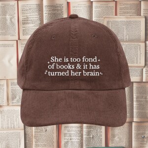 以下が含まれることがあります： 白い刺繍で「She is too fond of books & it has turned her brain」と書かれた、茶色のコーデュロイ製のベースボールキャップです。