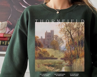 May include: Dark green sweatshirt with the word "THORNFIELD" printed at the top. The sweatshirt features a landscape painting of a castle and the text "TAKE A WALKING TOUR OF THE WILD MOORS", "HUNT FOR GHOSTS WITHIN THE MANOR HALLS", and "TIE THE KNOT IN OUR BEAUTIFUL CHAPEL".