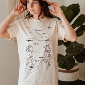 May include: A white t-shirt with a black and white illustration of a shoe patent design. The patent is for a "Tap and Tap Assembly for Dancers" and is dated July 26, 1938. The patent number is 2,124,908.