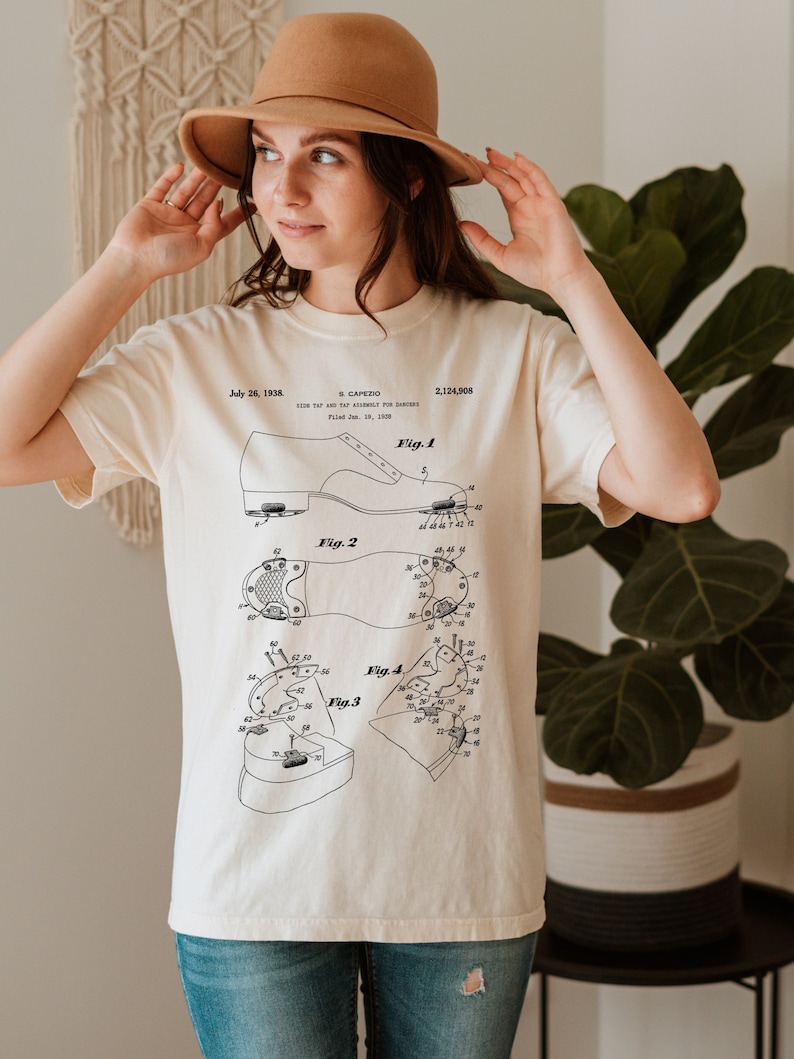 May include: A white t-shirt with a black and white illustration of a shoe patent design. The patent is for a "Tap and Tap Assembly for Dancers" and is dated July 26, 1938. The patent number is 2,124,908.