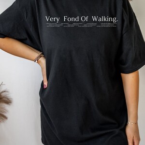 May include: Black oversized t-shirt with the text "Very Fond Of Walking." The text is in white and includes a list of phrases about walking.