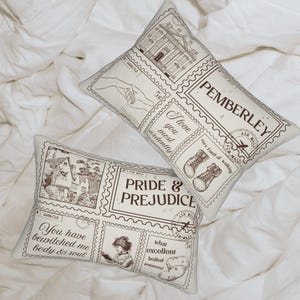 Op de afbeelding: Twee rechthoekige kussens met een vintage stempelontwerp. Eén kussen leest "PEMBERLEY" en de andere "PRIDE & PREJUDICE". De kussens hebben sepia-getinte illustraties en tekst, waaronder citaten en afbeeldingen van laarzen en gebouwen.