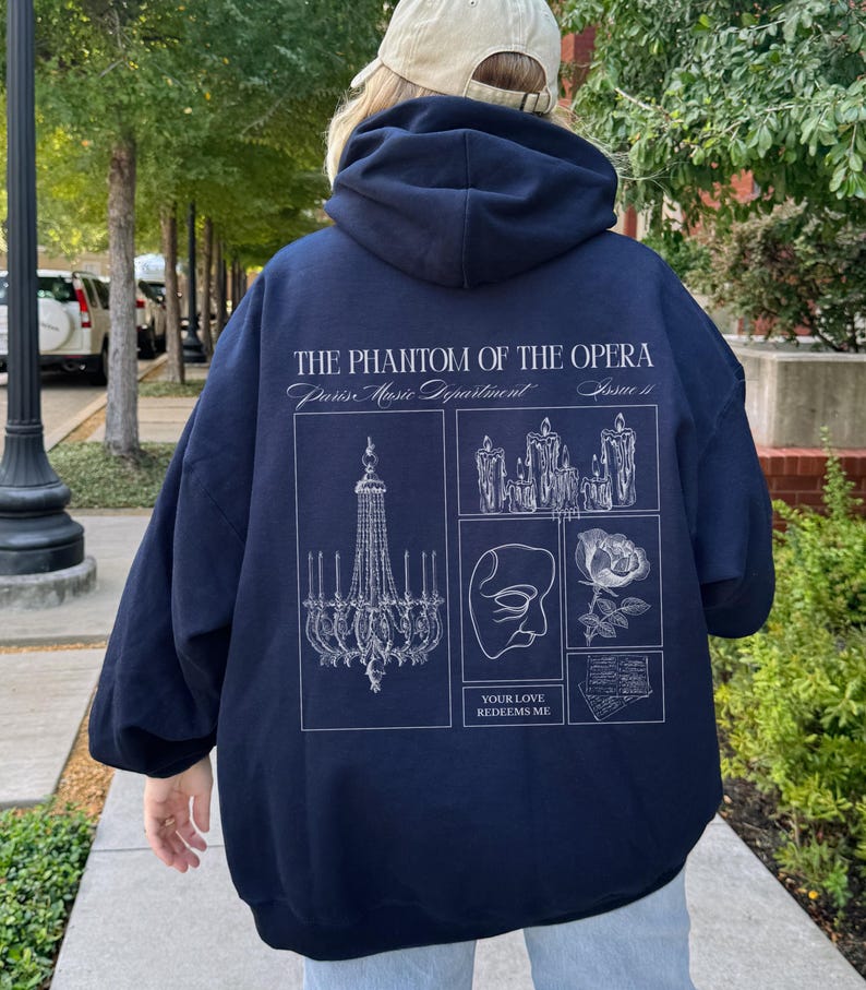 May include: Navy blue hoodie with a white graphic design featuring elements from "The Phantom of the Opera." The design includes a chandelier, candles, a mask, a rose, and the text "YOUR LOVE REDEEMS ME."