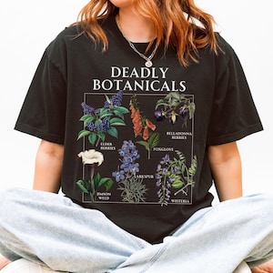 May include: Black t-shirt featuring the text "DEADLY BOTANICALS" above a botanical illustration of various plants, including Elderberries, Foxglove, and Jimson Weed. The shirt is a comfortable, casual style.