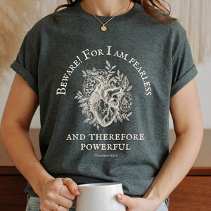May include: A dark gray t-shirt with a white graphic of a heart with flowers and the text "Beware! For I am Fearless and Therefore Powerful - Frankenstein".