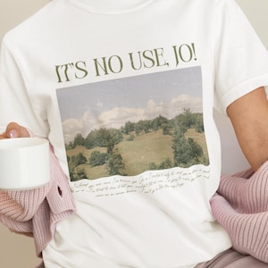 May include: White t-shirt with a vintage-style photo of a green landscape and the text "IT'S NO USE, JO!" printed on it.