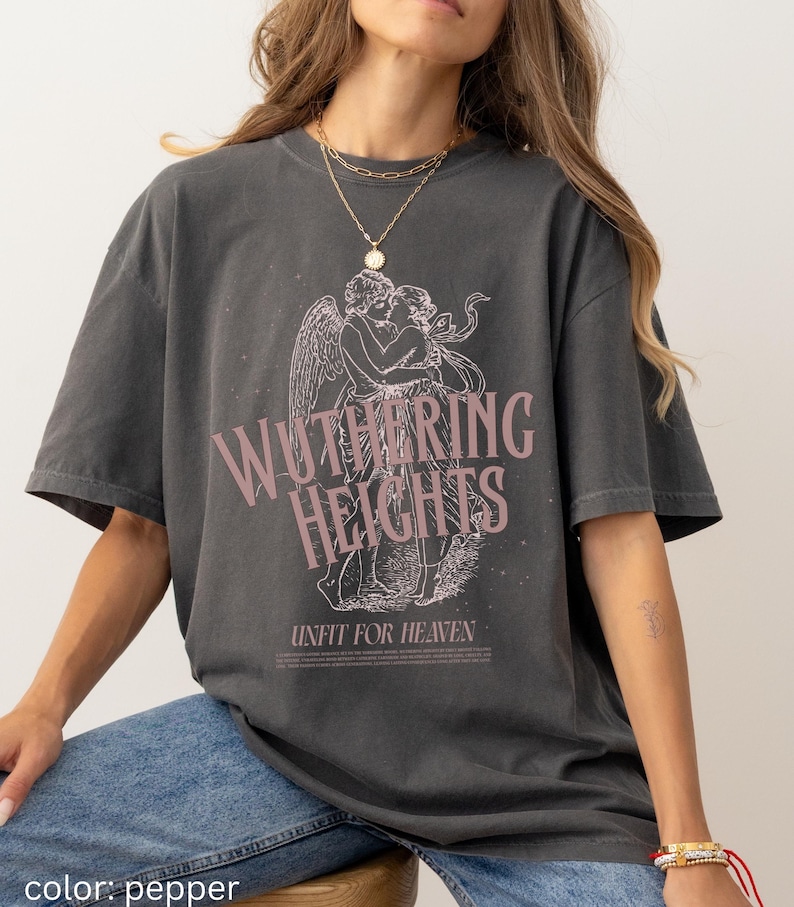 May include: Pepper-colored t-shirt featuring a graphic of two figures embracing with angel wings, and the text "Wuthering Heights" in a pink hue. Below the text is the phrase "Unfit for Heaven".