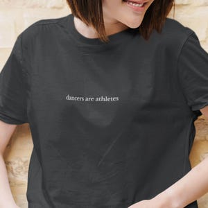 Puede incluir: Una camiseta negra recortada con el texto "dancers are athletes" en letras blancas.