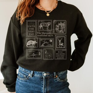 K&ouml;nnte beinhalten: Schwarzer Pullover mit einem wei&szlig;en Grafikdruck von Vintage-Briefmarken mit Illustrationen von Tieren und dem Text "Until the very end, The Marauders established 1971, Rule Breakers Mischief Makers".