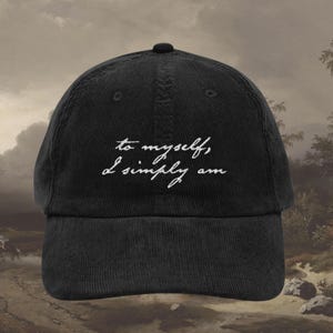 Puede incluir: Gorra de béisbol de pana negra con el texto bordado en blanco "to myself, I simply am". La gorra tiene una visera curva y un botón en la parte superior. El fondo es una pintura de paisaje.