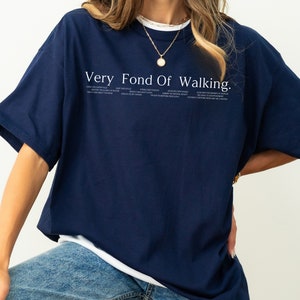 May include: A navy blue t-shirt with a white graphic that says "Very Fond Of Walking." The graphic also includes a list of phrases about walking.