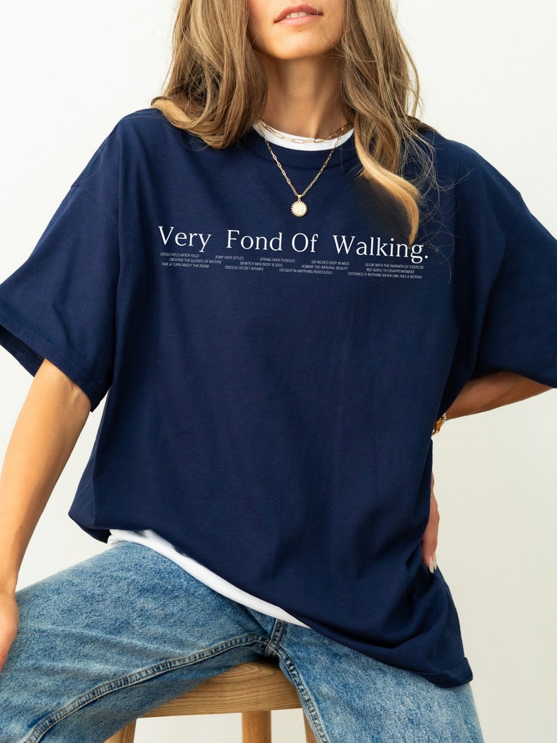 May include: A navy blue t-shirt with a white graphic that says "Very Fond Of Walking." The graphic also includes a list of phrases about walking.