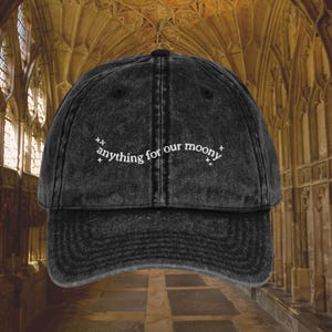 May include: A black denim baseball cap with white embroidered text that reads "anything for our moony".
