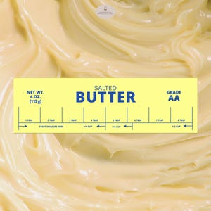 Puede incluir: Primer plano de mantequilla amarilla en espiral con una etiqueta amarilla. La etiqueta dice "SALTED BUTTER" y "GRADE AA". También indica medidas de 1 cucharada a 1/2 taza, y el peso neto es de 113g.