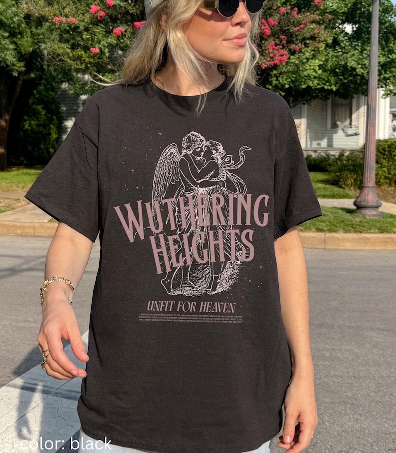 May include: Black t-shirt featuring the text "Wuthering Heights" in a stylized font, with an illustration of two figures embracing. Below the text is the phrase "Unfit For Heaven". The shirt is a dark color.