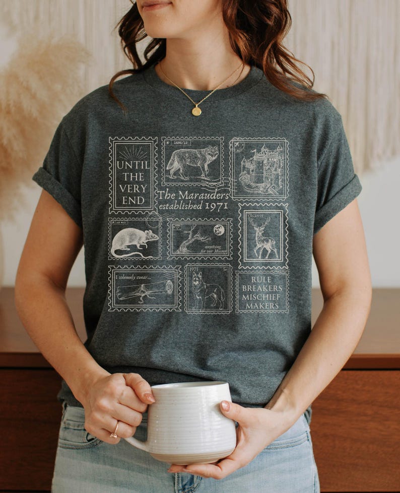 May include: A dark gray t-shirt with a white graphic print of stamps featuring illustrations of a wolf, a castle, a rat, a tree, a deer, a lizard, a dog, and text that reads "Until the very end. The Marauders established 1971. Rule Breakers Mischief Makers."