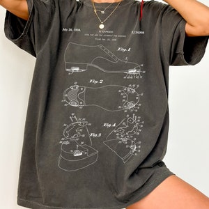 May include: A charcoal grey oversized t-shirt with a vintage patent design for a tap and tap assembly for dancers. The patent number is 2,124,908 and the date is July 26, 1938.