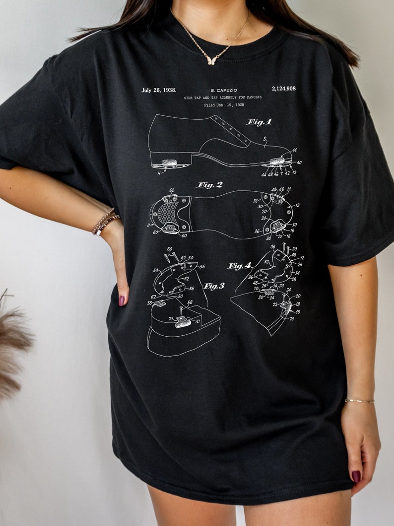 May include: Black t-shirt with a white print of a patent design for a shoe tap assembly for dancers. The patent number is 2,124,908 and the date is July 26, 1938. The text "S. Capezio" is also printed on the shirt.